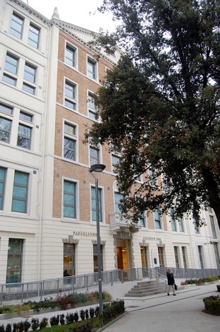Lapide commemorativa situata su un edificio storico, con dettagli architettonici e vegetazione circostante.