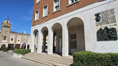 Lapide commemorativa affissa su un edificio, con archi in marmo e contesto urbano.