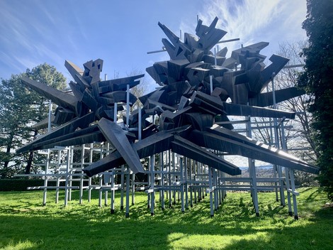 Monumento alla Resistenza con struttura poligonale nera e diagonali in acciaio, immerso nel verde.