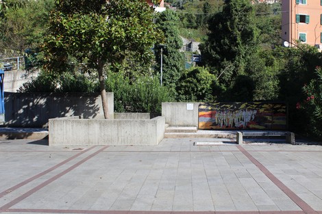 Vista del Monumento alla Resistenza, con struttura in cemento, piante e una murale sullo sfondo.