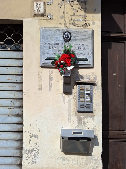 Lapide commemorativa di Duò, adornata con fiori, su una parete storica di un edificio.