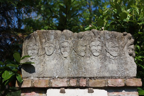 Monumento ai partigiani di Ca' di Bue con rilievi di volti e dettagli ornamentali, circondato da vegetazione.