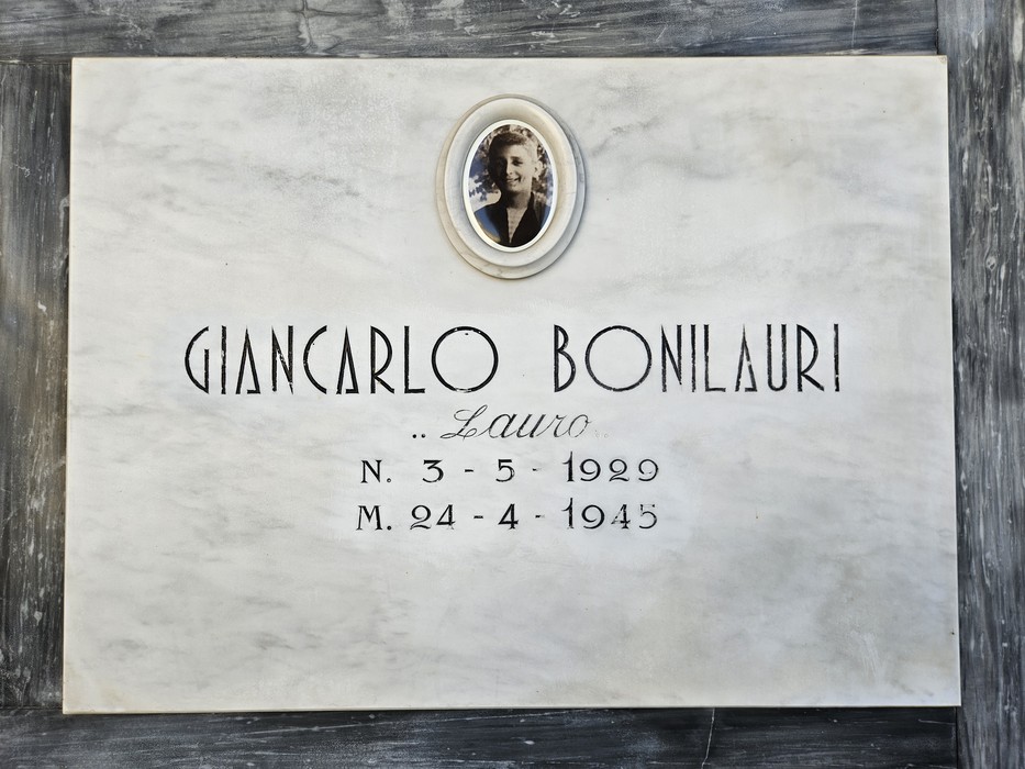 Lapide in marmo con ritratto ovale fotografico e iscrizione dedicata a un caduto.