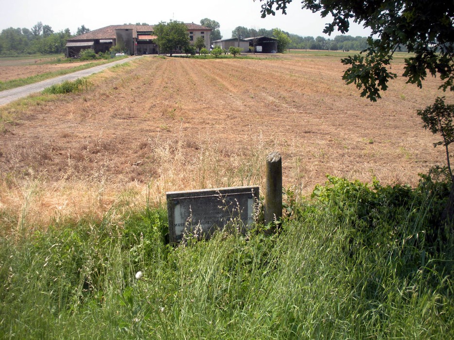 Cippo commemorativo a Casonato e Muselli, immerso in un paesaggio rurale con campi e vegetazione.
