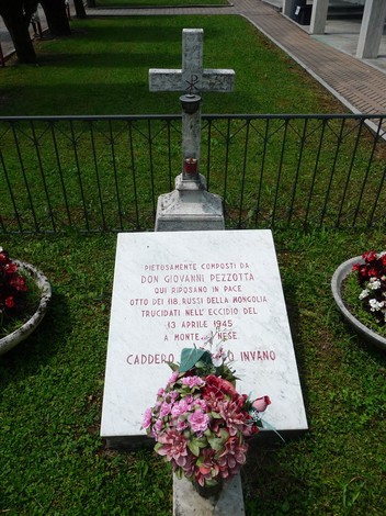 Sepolcro di otto russi, con una lapide commemorativa e fiori, immerso in un'area verde e curata.