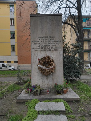 Monumento commemorativo ai partigiani uccisi a San Ruffillo, ricco di piante e un omaggio floreale.