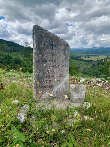 Cippo commemorativo dedicato a Agostini, Bussolaro e Fontana, immerso nella natura montana.