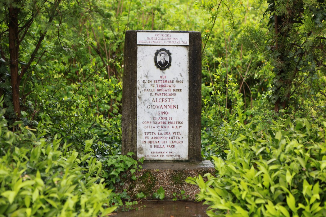 Cippo commemorativo dedicato a Alceste Giovannini, immerso nel verde, con inscriptioe a lui dedicata.