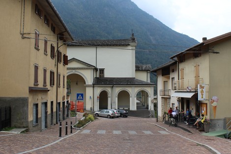 Vista del "Monumento ai Martiri della Libertà" in un contesto urbano, circondato da case e montagne.
