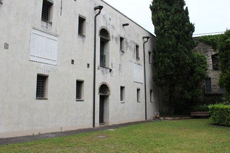Stele commemorativa in un'area verde, affiancata da edifici storici e alberi.