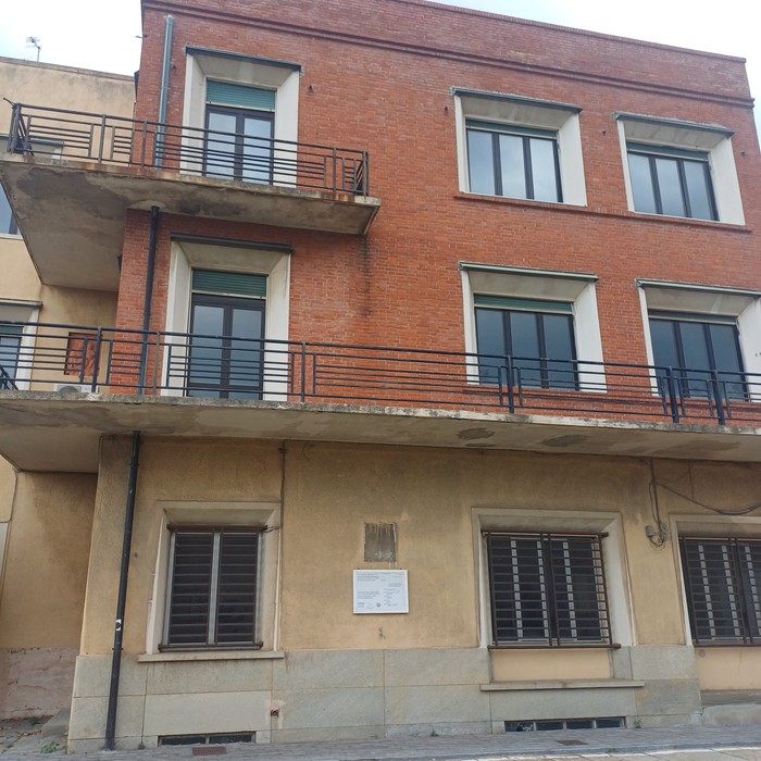 Palazzina a tre piani, targa con iscrizione affissa sulla facciata intonacata al piano terra.