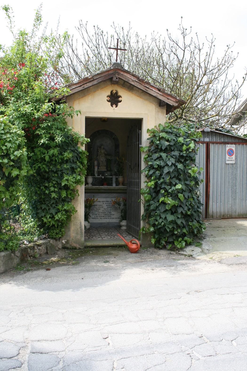 Tabernacolo di Rosi immerso nel verde, con ingresso ornato da piante e una statua al suo interno.