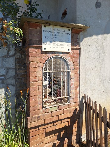 Lapide commemorativa in mattoni con grata, dedicata a Robotti e Perotti, situata in un ambiente rurale.