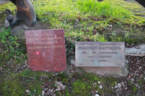 Monumento a Matteotti con placche commemorative in un contesto naturale e verdeggiante.