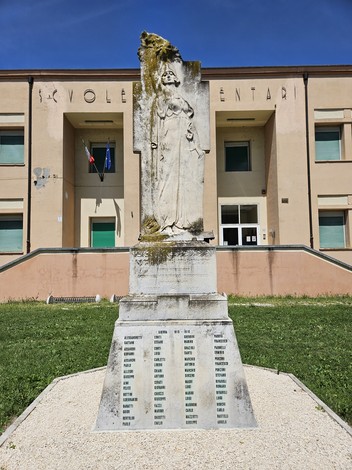 Monumento ai Caduti con statua e liste commemorative, situato davanti a un edificio scolastico.
