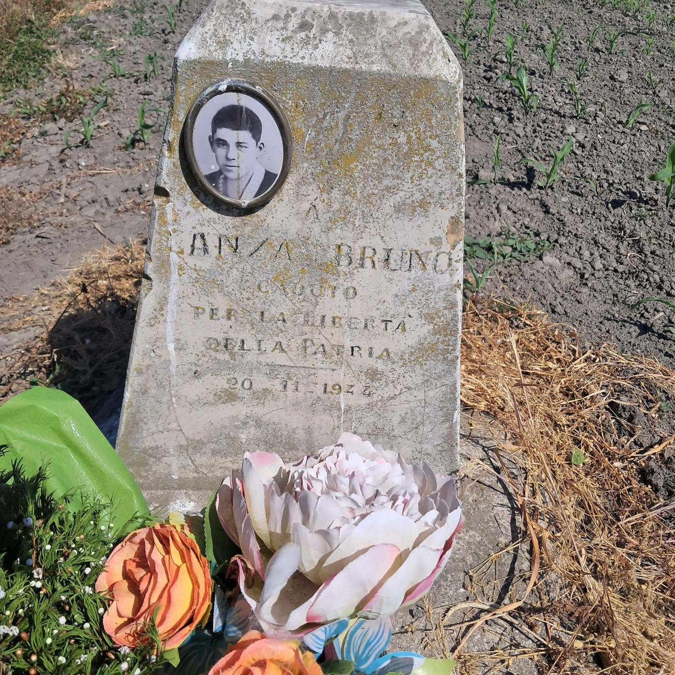Cippo commemorativo dedicato a Bruno Lanza, simbolo della resistenza e della liberazione. Decorato con fiori.