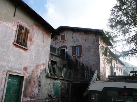 Edificio rustico con pareti scrostate e balconi in legno, immerso in un ambiente montano.