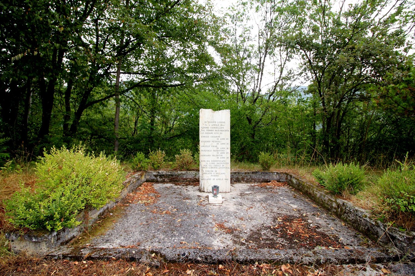 Cippo commemorativo in memoria dei partigiani uccisi a Colle di Postignano, immerso nella natura.
