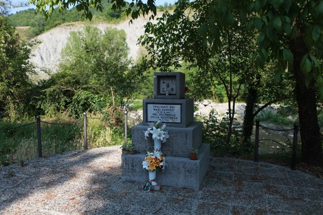 Monumento ai partigiani fucilati, circondato da vegetazione, con decorazioni floreali. Un luogo di memoria e rispetto.