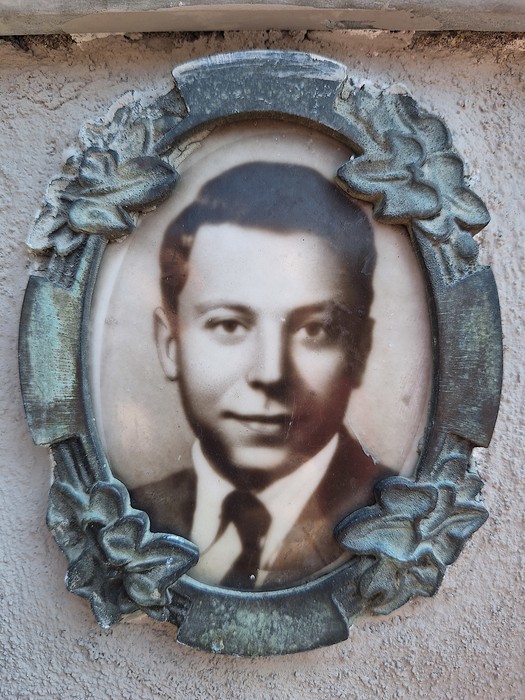 Ritratto ovale di un giovane uomo in giacca e cravatta, entro una cornice in metallo decorata a fiori.