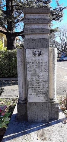 Cippo commemorativo su strada con iscrizioni, immerso nel verde, rappresenta un simbolo storico locale.