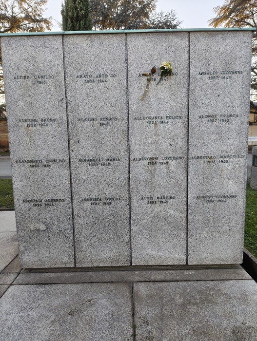 Monumento commemorativo al "Campo della Gloria" con nomi incisi su lastre di pietra e omaggio floreale.