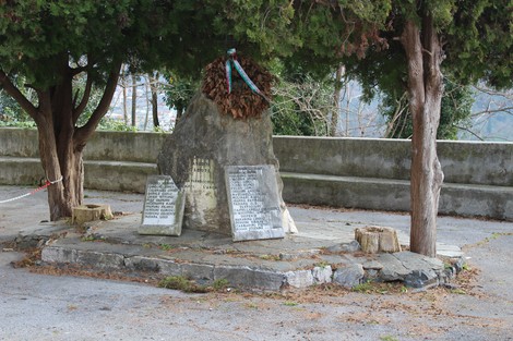 Monumento ai caduti di Morego, circondato da alberi, con pietra centrale e due lapidi commemorative.