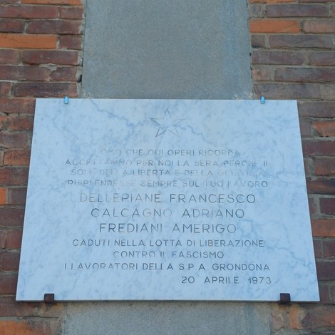 Lapide marmorea con stella e iscrizione, fissata su pilastro tra due pareti in mattoni.