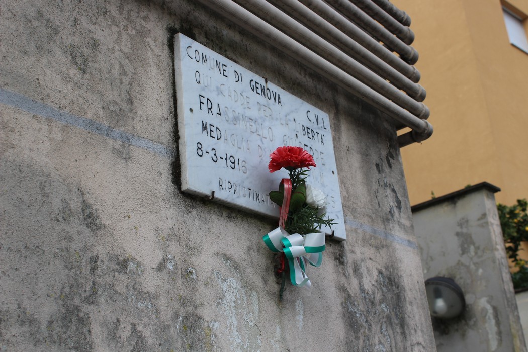Lapide commemorativa a Frassinello, con un omaggio floreale e una dedica sul muro.