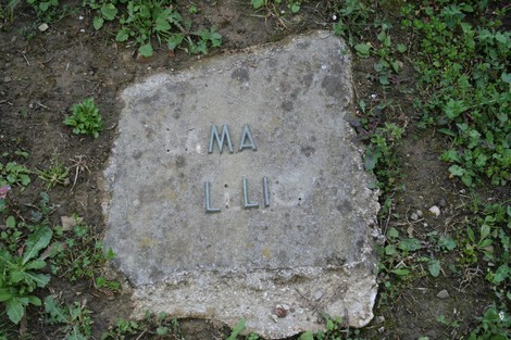 Monumento del cimitero di Stia, con lapide in pietra circondata da erba e fiori.