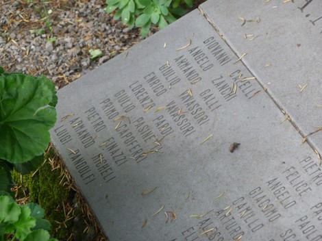 Lapide commemorativa per i partigiani a Ambiveri, con nomi incisi e decorazioni floreali circostanti.