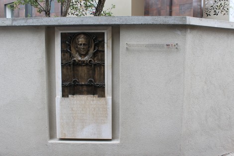 Monumento a D'Amico, con un busto scolpito e una base su muro di pietra chiara.