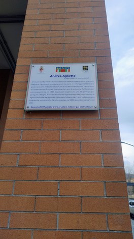Targa commemorativa dedicata ad Andrea Aglietto, affissa su un muro in mattoni.