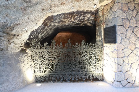 Ingresso alle Fosse Ardeatine, con una cancellata artistica in metallo e un ambiente roccioso circostante.