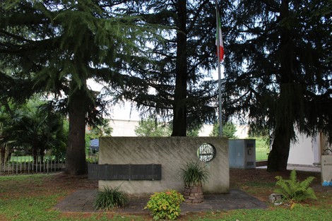 Monumento alla Resistenza immerso nel verde, con bandiera italiana e varie piante circostanti.