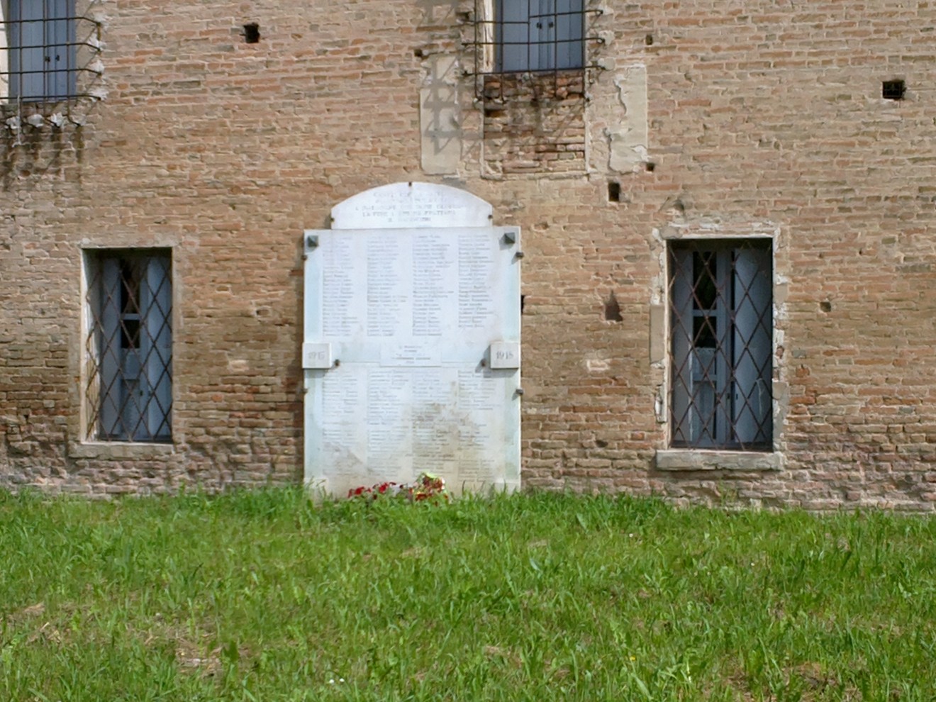 Lapide commemorativa dedicata ai caduti di Reggiolo, posizionata su un muro di mattoni, circondata da erba.