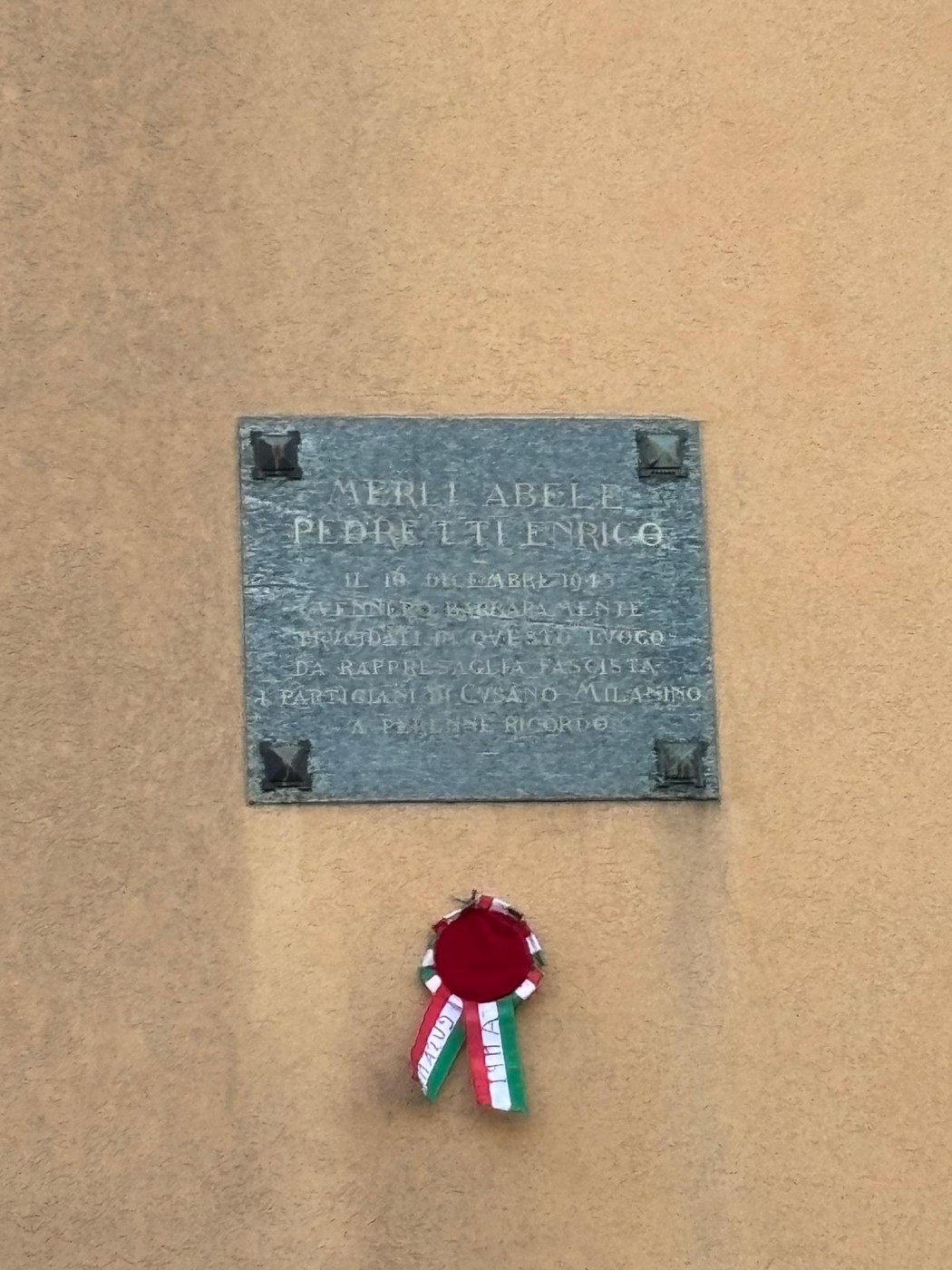Lapide commemorativa in memoria di Merli e Pedretti, decorata con una corona di alloro e i colori nazionali.