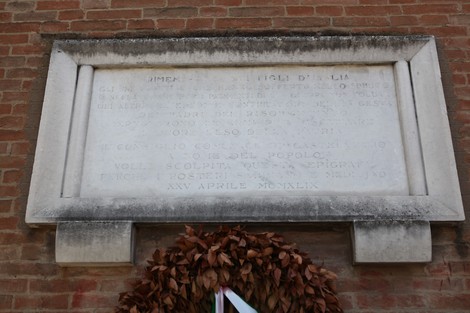 Lapide commemorativa con iscrizioni su fondo marmoreo, posizionata su un muro di mattoni.