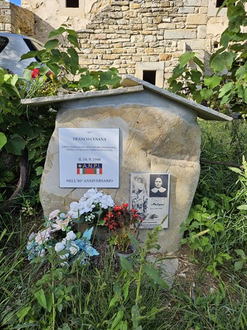 Cippo commemorativo dedicato a Franco Cesana, con foto e fiori, immerso nella natura.