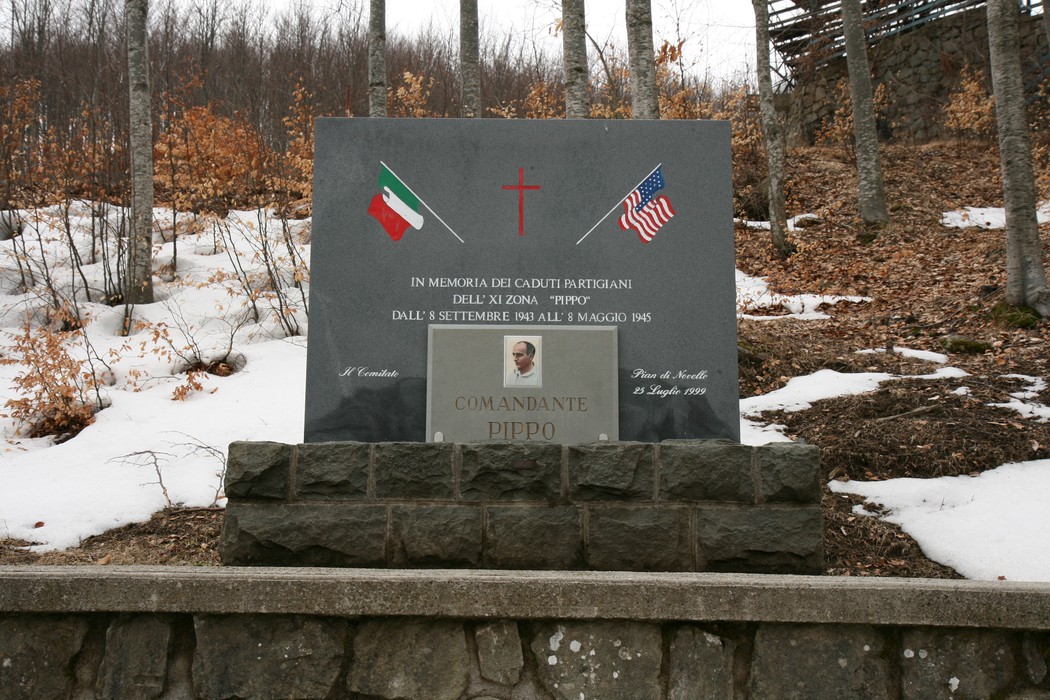 Monumento in memoria del comandante Pippo, con bandiere italiana e americana tra boschi innevati.