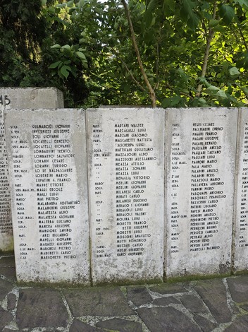 Monumento ai Caduti con una fila di nomi incisi su lastre di pietra, in un contesto verde e tranquillo.