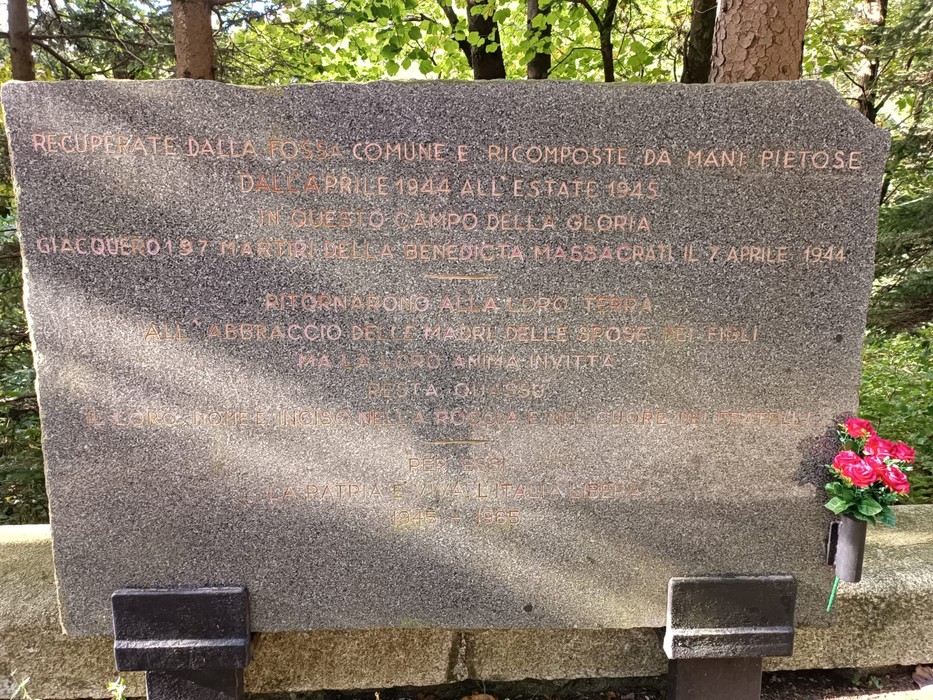 Memoriale dedicato ai caduti della Benedicta, situato in un ambiente boschivo, con fiori artificiali.