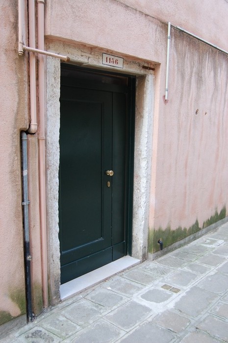 Porta verde in un vicolo, con pareti rosa e pavimento in pietra, che richiama l'atmosfera di un luogo storico.