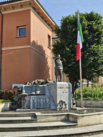 Monumento ai Caduti a San Rocco al Porto, con statua, bandiera italiana e elementi commemorativi.