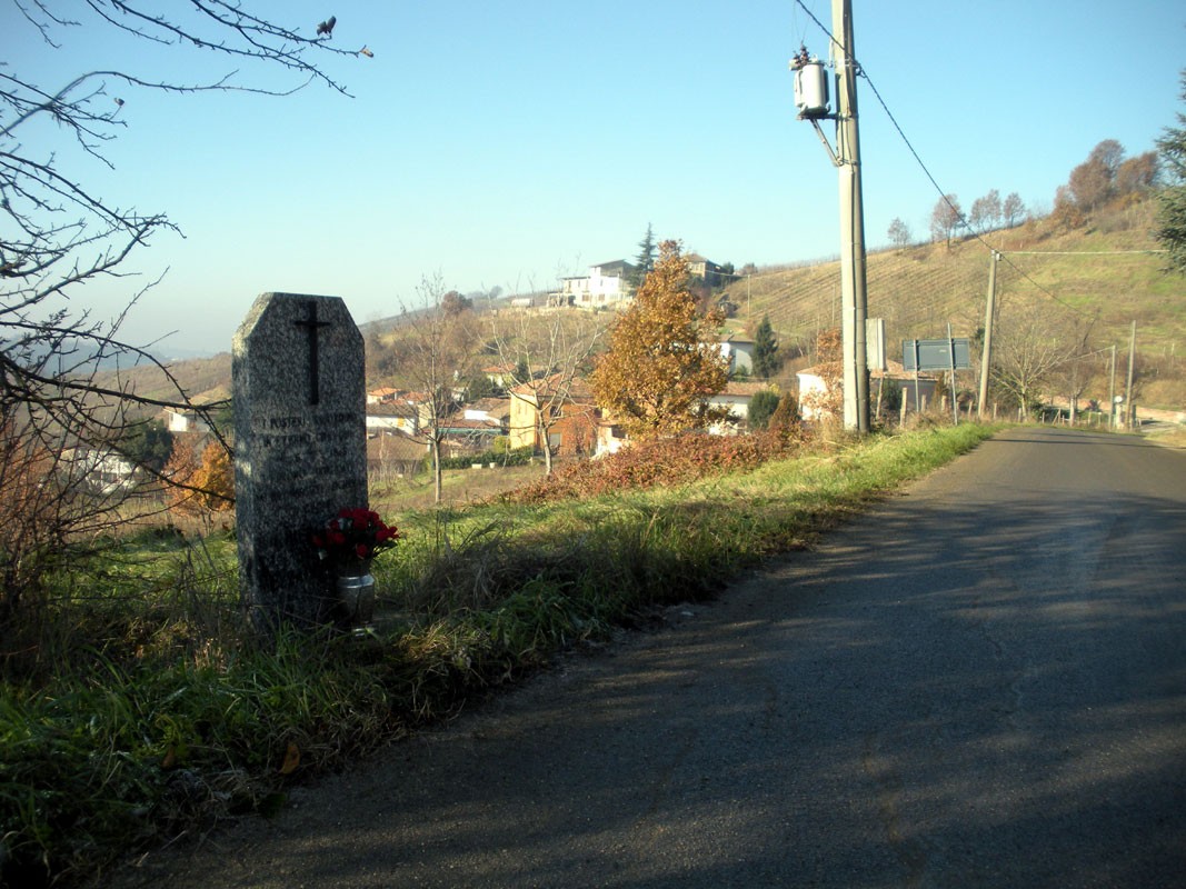 Cippo commemorativo in un paesaggio rurale, con vista su una collina e case.