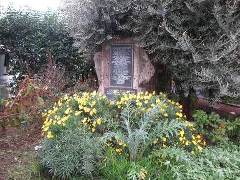Lapide commemorativa nel verde, dedicata alla memoria degli eventi di Peretola. Fiori colorati la circondano.