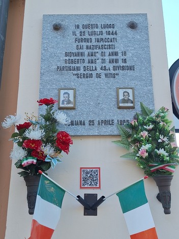 Lapide commemorativa dedicata ai fratelli Amè, con foto e decorazioni floreali.