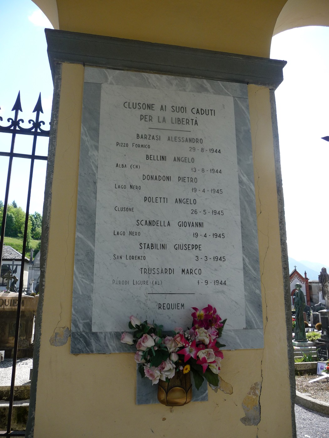Lapide commemorativa ai caduti partigiani con nomi e date in onore della libertà. Decorata con fiori.