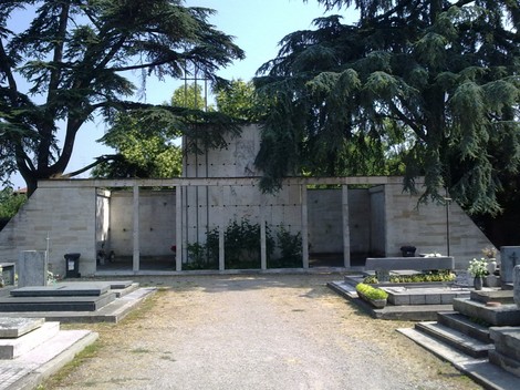 Monumento ai Caduti Partigiani, struttura in cemento con alberi e tombe circostanti in un ambiente sereno.