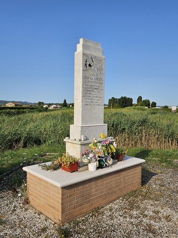 Monumento ai Martiri di Ponte Ruffio, con decorazioni floreali e una cornice naturale di verde.